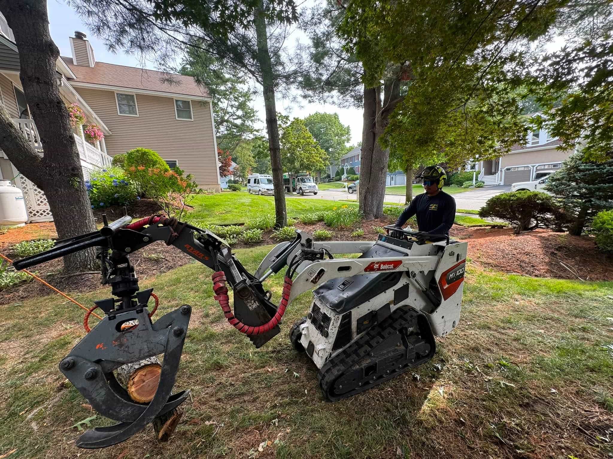 Tree removal equipment featuring a mini track loader with a grapple attachment moving heavy logs during a residential tree removal project by Juarez Landscaping and Tree Services.