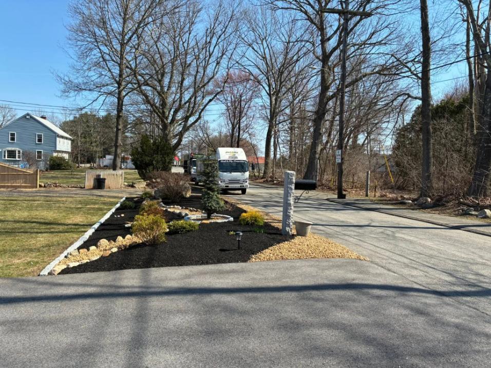 Landscape bed design with mulch, stone edging, shrubs, and an ornamental tree by a residential driveway